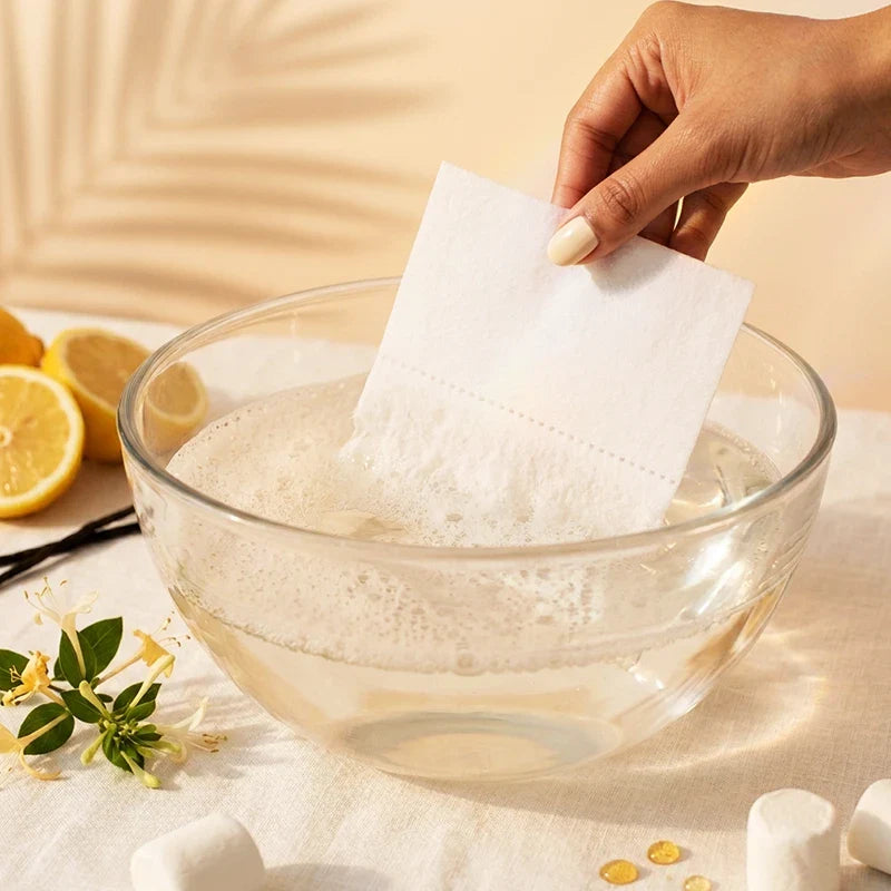 QLEAN Sweet Summer Love detergent sheet dissolving in clear glass bowl of warm water with foam bubbles
