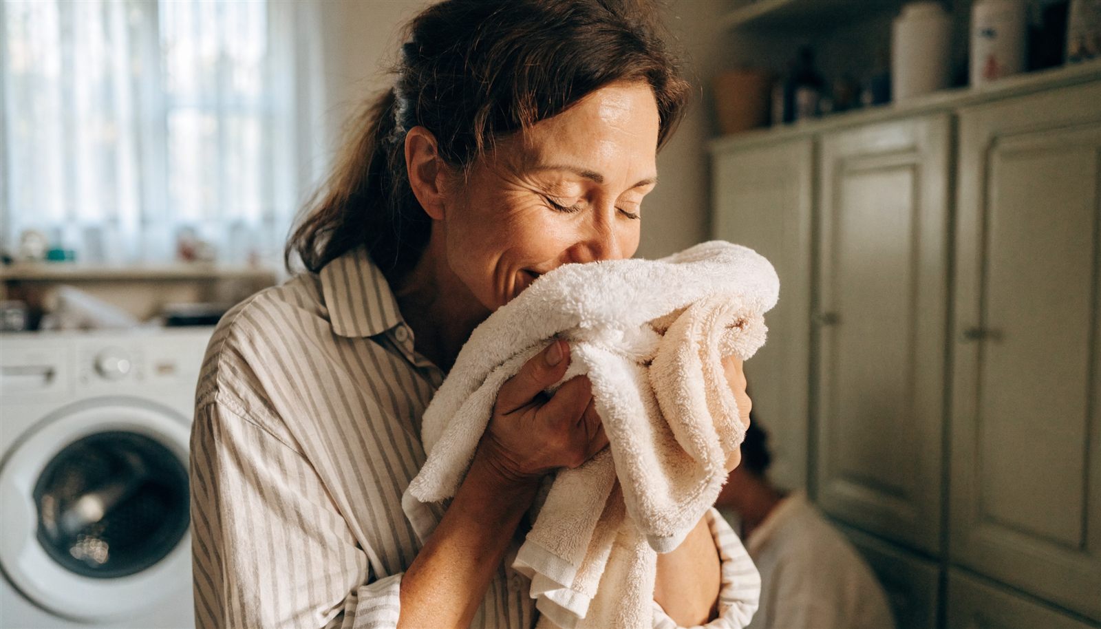 A mom holding a stack of fresh laundry to her face, smiling at how good it smells